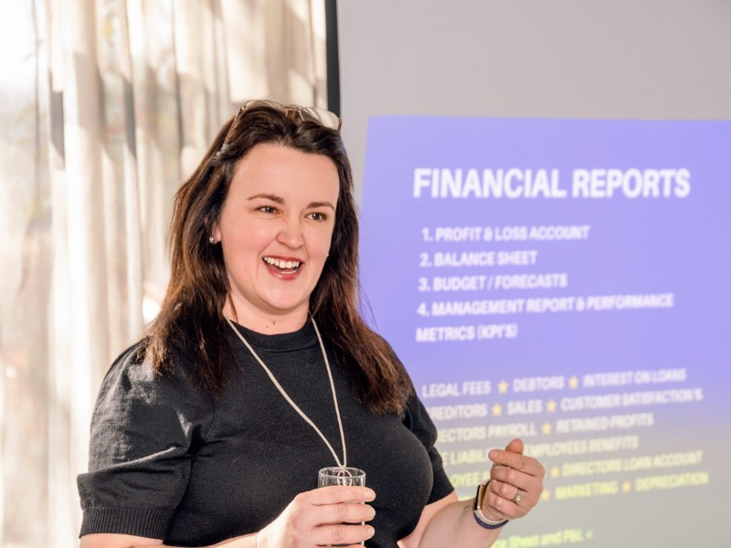 Pauline Healey standing in front of her presentation about financial reports on a big screen behind her.