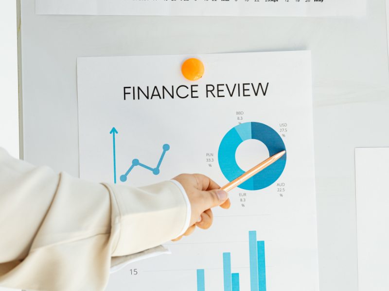 A hand points at a finance review chart