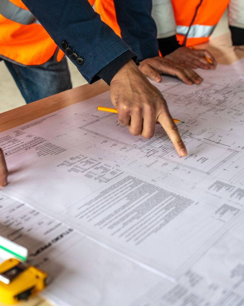2 workers wearing orange hi-viz vests stand over a huge inventory rolled out on a desk