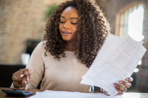 A lady holds a piece of paper as she taps the calculator