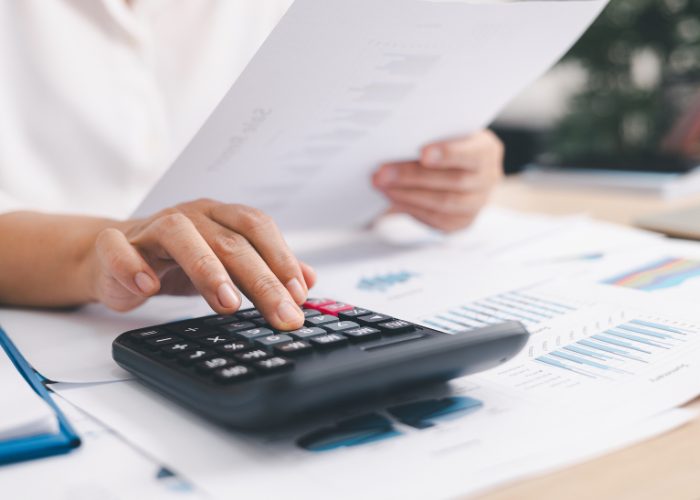 A hand taps out figures on a calculator whilst holding sheets paper