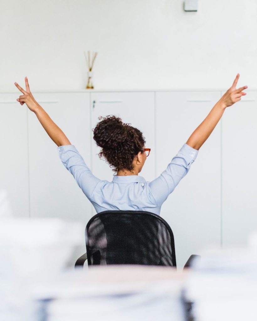Picture taken from behind a lady sitting in her office chair and throwing her hands up in celebration after a financial clarity call